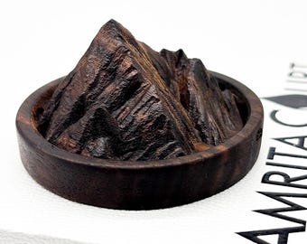 May include: A dark brown wooden mountain sculpture with a detailed, textured surface. The sculpture is placed in a round, dark brown wooden bowl.