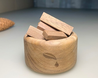 Puede incluir: Un cuenco de madera con un diseño de hoja y una gota de agua, lleno de pequeños palitos de madera para aromaterapia.