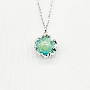 May include: A silver necklace with a round pendant. The pendant has a blue and gold glass orb, held in a decorative silver frame. The chain is a delicate silver link. The necklace is shown against a white background.