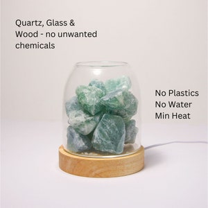 K&ouml;nnte beinhalten: Eine Glasglocke mit einem Holzsockel, die gr&uuml;ne Fluoritkristalle enth&auml;lt. Der Text "No Plastics No Water Min Heat" ist auf der rechten Seite des Bildes sichtbar. Der Text "Quartz, Glass & Wood - no unwanted chemicals" ist oben im Bild sichtbar.