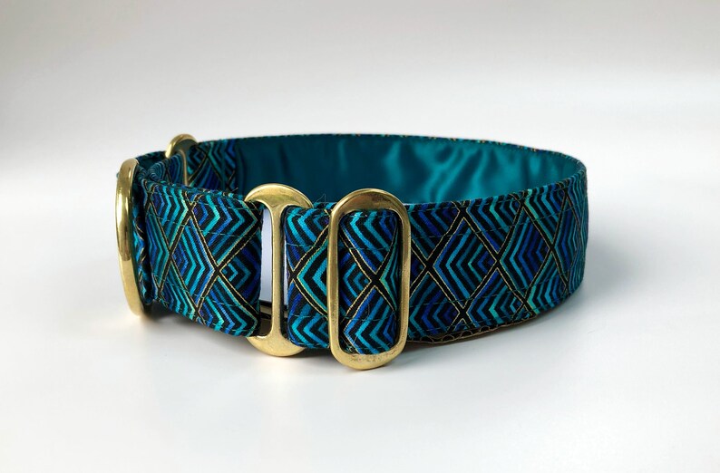 Pu&ograve; includere: Un collare per cani blu turchese con un motivo geometrico in tonalit&agrave; di blu, verde e oro. Il collare ha due anelli a D in ottone.