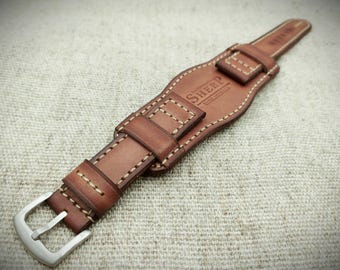 May include: A brown leather watch strap featuring a wide cuff design with light-coloured contrast stitching. The strap includes a silver-toned metal buckle and is embossed with the text SHERP in the centre of the leather cuff section.