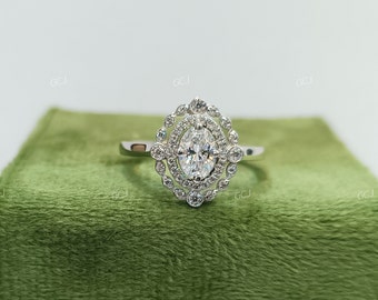 May include: A silver ring with a large oval-shaped diamond surrounded by a halo of smaller diamonds. The ring is set on a green velvet cushion.