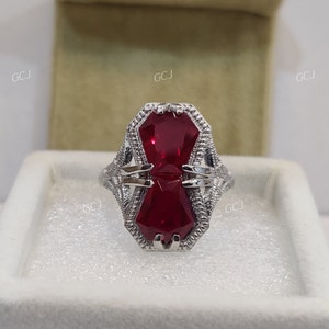 Peut inclure: Une bague en argent avec une grande pierre rouge octogonale. La bague est sertie dans un design délicat et orné.