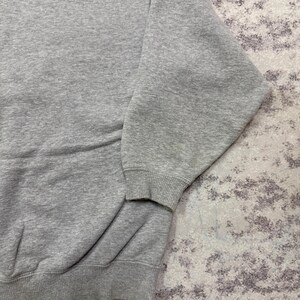 May include: A heather gray sweatshirt with ribbed cuffs and hem. The long sleeves are visible, and the fabric appears to be a soft, comfortable material. The sweatshirt is a casual garment.