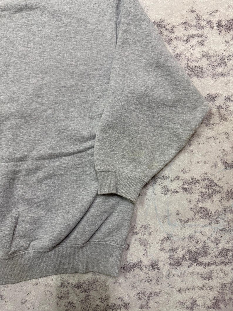 May include: A heather gray sweatshirt with ribbed cuffs and hem. The long sleeves are visible, and the fabric appears to be a soft, comfortable material. The sweatshirt is a casual garment.