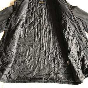 May include: A black jacket with a quilted interior lining featuring a diamond pattern. The garment includes a full-length front zipper closure, a collar, and a brand label located at the inner neckline. The outer shell is a solid black fabric.