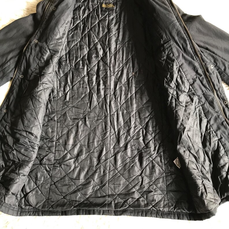 May include: A black jacket with a quilted interior lining featuring a diamond pattern. The garment includes a full-length front zipper closure, a collar, and a brand label located at the inner neckline. The outer shell is a solid black fabric.