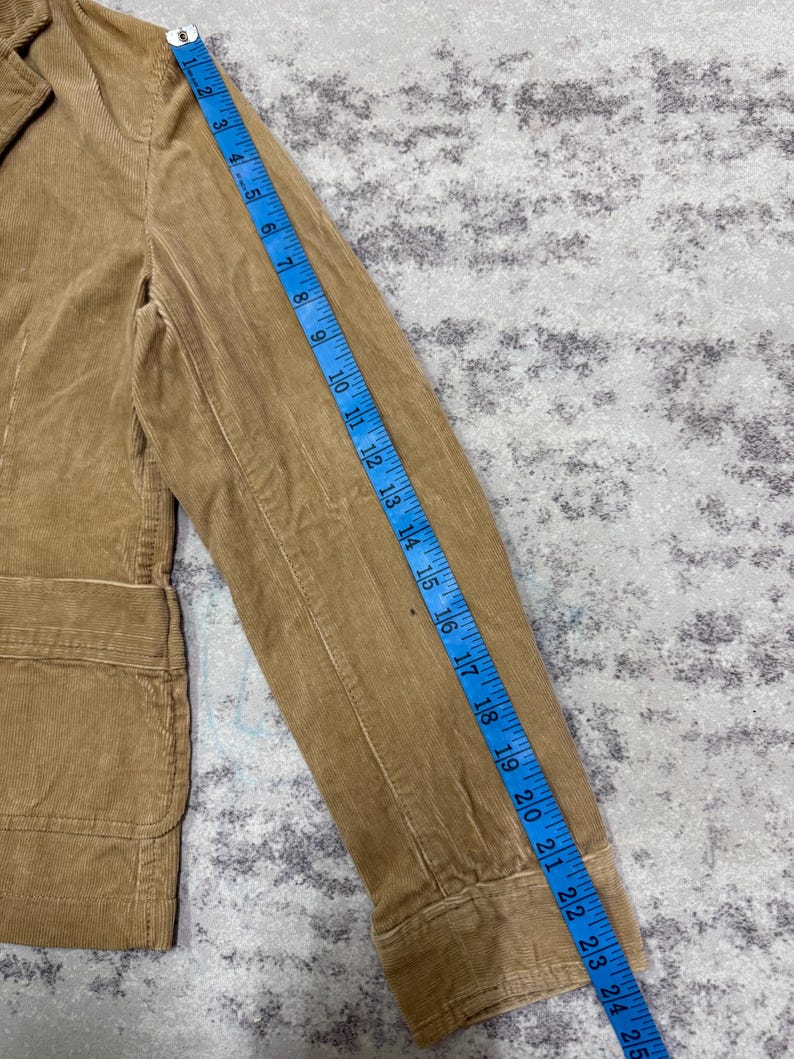 Puede incluir: Blazer de pana color beige con solapa de muesca y dos bolsillos delanteros. La longitud de la manga es de aproximadamente 63.5 cm, medida con una cinta m&eacute;trica azul. Dise&ntilde;o cl&aacute;sico y entallado.