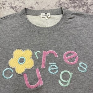 May include: A gray sweatshirt with a crew neck and embroidered floral and text design. The design features a yellow flower with a blue center and the word "cures" in pink, green, and blue lettering.