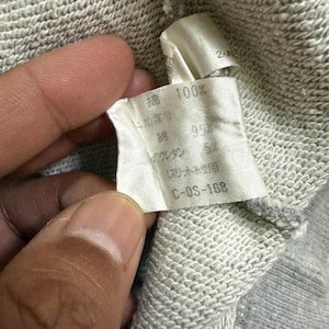 May include: Close-up of a fabric tag with Japanese text and numbers. The tag is white with black text, showing fabric composition: 100% cotton, 95% cotton, and 5% polyurethane. The tag is attached to a gray fabric.