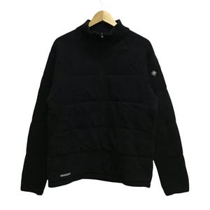 May include: Black quilted jacket with a high collar and a half-zip closure. The jacket has long sleeves and a small logo patch on the upper left sleeve. The jacket is hanging on a wooden hanger.