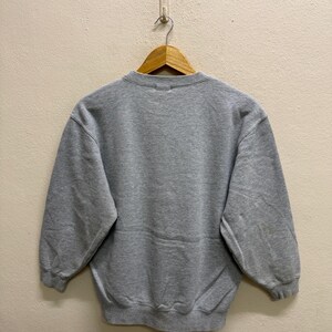 May include: A heather gray sweatshirt with a crew neck and long sleeves. The sweatshirt is hanging on a wooden hanger against a neutral wall. The garment appears to be made of a soft, comfortable material.