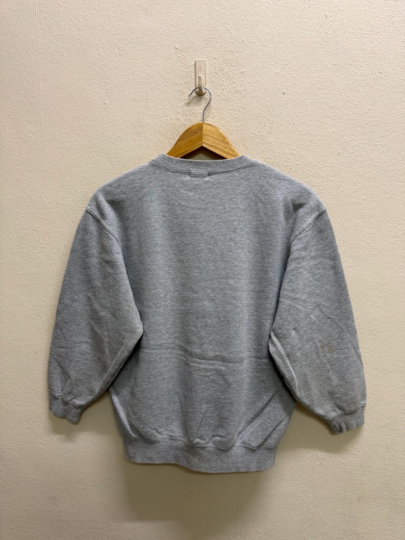 May include: A heather gray sweatshirt with a crew neck and long sleeves. The sweatshirt is hanging on a wooden hanger against a neutral wall. The garment appears to be made of a soft, comfortable material.