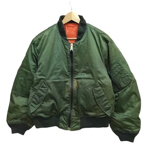 May include: A green bomber jacket with a black zipper and ribbed cuffs and hem. The jacket has two front pockets and a black collar. The interior lining is orange. The jacket is hanging on a wooden hanger.