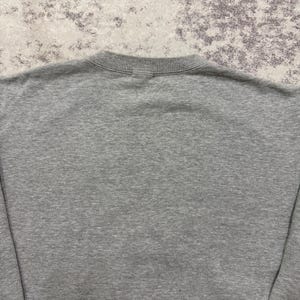 May include: A heather gray sweatshirt with a crew neck. The fabric appears to be a soft, knit material. The image shows the back of the sweatshirt, with the neckline and upper back visible.