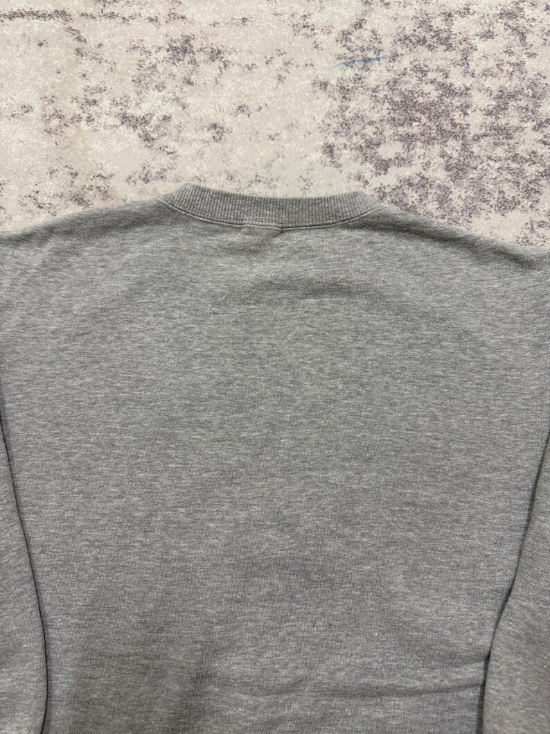 May include: A heather gray sweatshirt with a crew neck. The fabric appears to be a soft, knit material. The image shows the back of the sweatshirt, with the neckline and upper back visible.