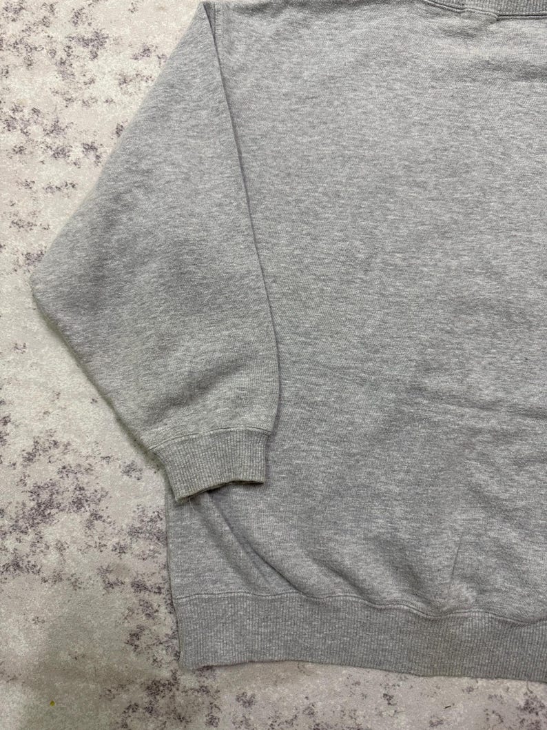 May include: A heather gray sweatshirt with ribbed cuffs and hem. The long sleeves and crew neck design offer a classic, casual look. The fabric appears to be a soft, medium-weight material, suitable for cooler weather.