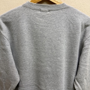 May include: A heather gray sweatshirt with a crew neck, hanging on a wooden hanger. The sweatshirt has a simple, minimalist design, with a focus on the soft, textured fabric. The sleeves are long and the overall style is casual.