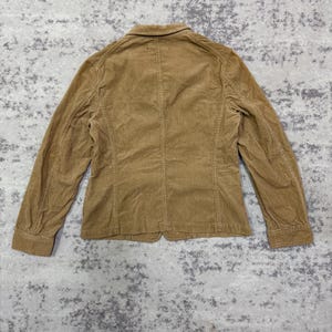 Puede incluir: Blazer de pana marr&oacute;n claro, visto desde atr&aacute;s. La chaqueta tiene un dise&ntilde;o cl&aacute;sico con cierre de bot&oacute;n y mangas largas. La tela de pana tiene una textura acanalada. El blazer es de color neutro.