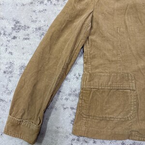 Puede incluir: Chaqueta de pana color marr&oacute;n claro con un dise&ntilde;o cl&aacute;sico. La chaqueta presenta un cuello con muescas, mangas largas y un bolsillo delantero. La tela tiene una textura acanalada y la chaqueta parece estar en buen estado.