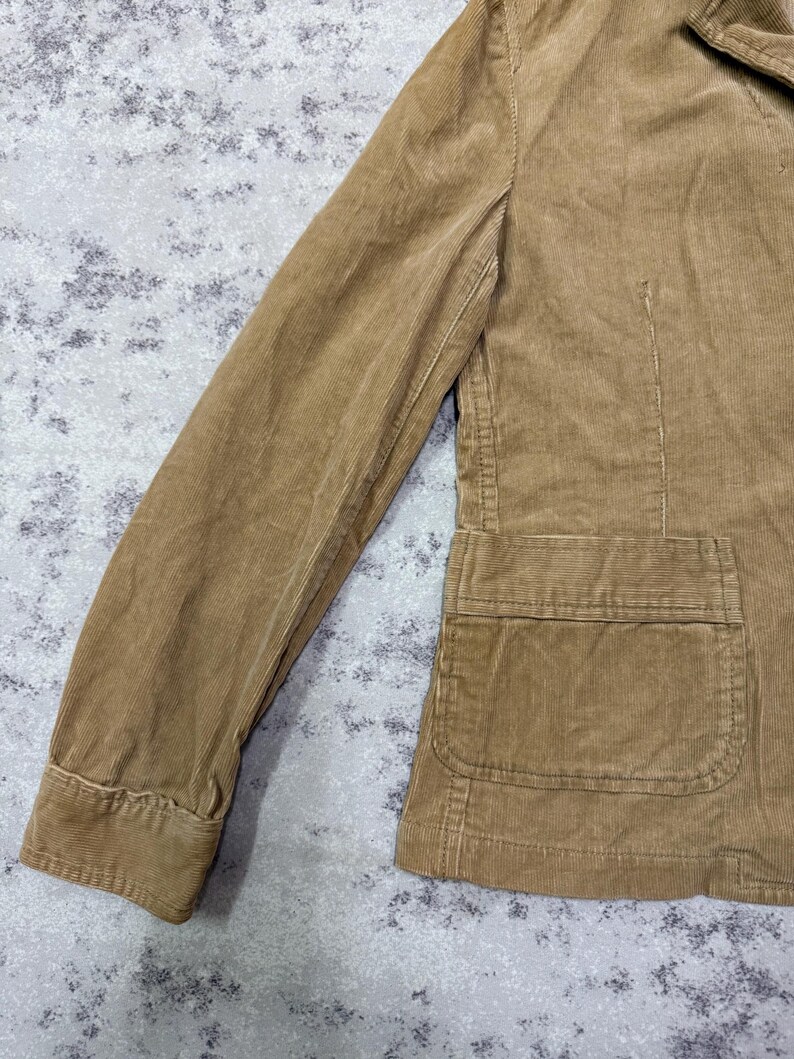 Puede incluir: Chaqueta de pana color marr&oacute;n claro con un dise&ntilde;o cl&aacute;sico. La chaqueta presenta un cuello con muescas, mangas largas y un bolsillo delantero. La tela tiene una textura acanalada y la chaqueta parece estar en buen estado.