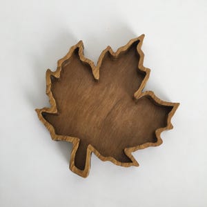Peut inclure: Un plateau en bois en forme de feuille avec un motif sculpté. Le plateau est en bois brun foncé et a une surface lisse et polie. Les bords du plateau sont légèrement surélevés, créant un bol peu profond. C'est un objet décoratif.