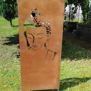 Könnte beinhalten: Ein rostiger Metall-Gartensichtschutz mit einem ausgeschnittenen Design eines Buddha-Gesichts. Der Sichtschutz ist braun und hat eine verwitterte Optik.