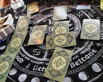 May include: A black velvet cloth with a circular design featuring a moon cycle and various dates.  There are eight green cards with a stylized letter 'D' and 'W' on each card.  The cards are arranged in a circle around the center of the cloth.  There are four lit tealight candles on the cloth.