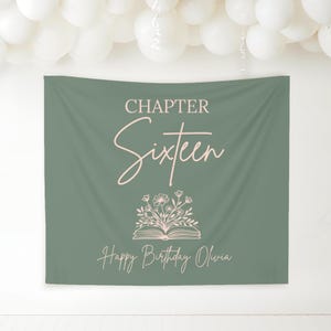 May include: A sage green fabric banner with the words "CHAPTER Sixteen" in a cursive font. Below the text is an open book with floral accents, and the words "Happy Birthday Olivia" are at the bottom. White balloons are in the background.