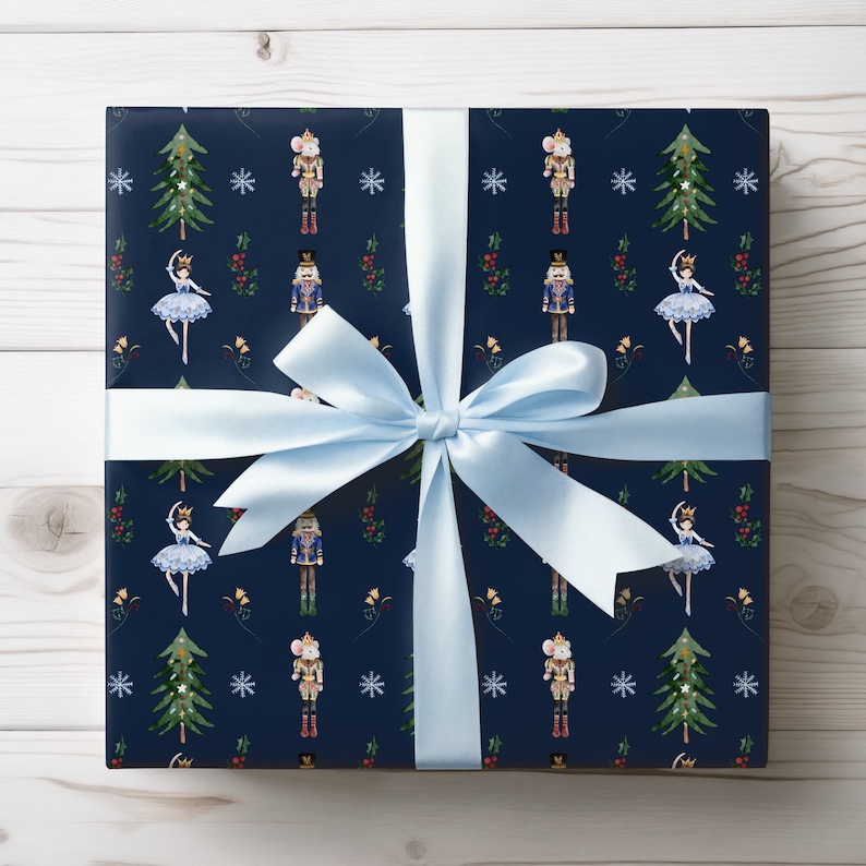 May include: A wrapped gift with navy blue wrapping paper featuring a repeating pattern of Christmas trees, snowflakes, nutcrackers, mice, and ballerinas. A light blue satin ribbon is tied in a bow around the gift.