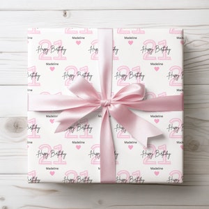 May include: White gift wrap with a pink and white repeating pattern of the number 21, the words "Happy Birthday" and the name "Madeline".