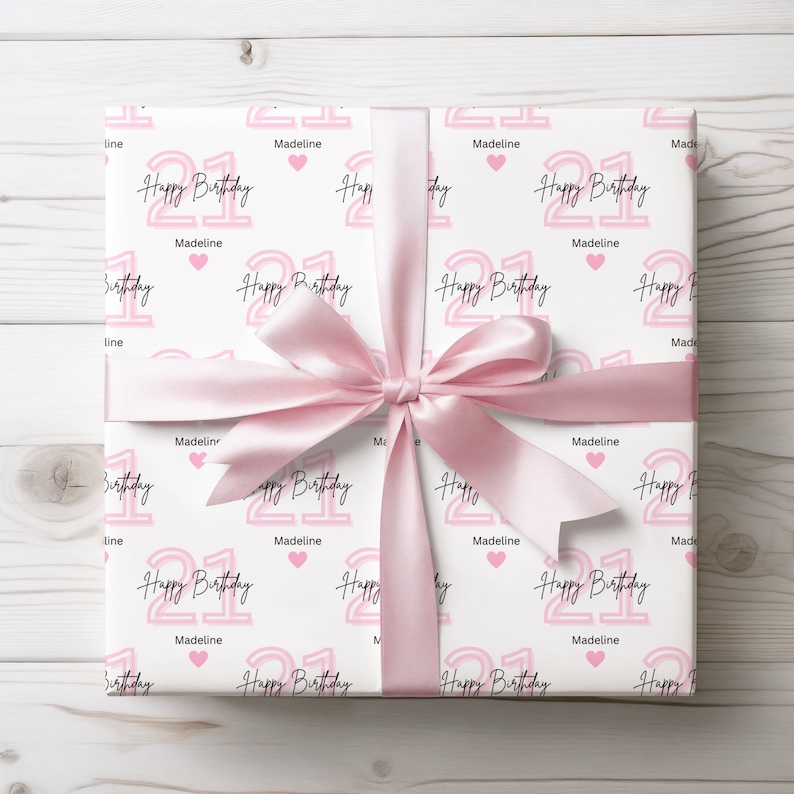 May include: White gift wrap with a pink and white repeating pattern of the number 21, the words "Happy Birthday" and the name "Madeline".