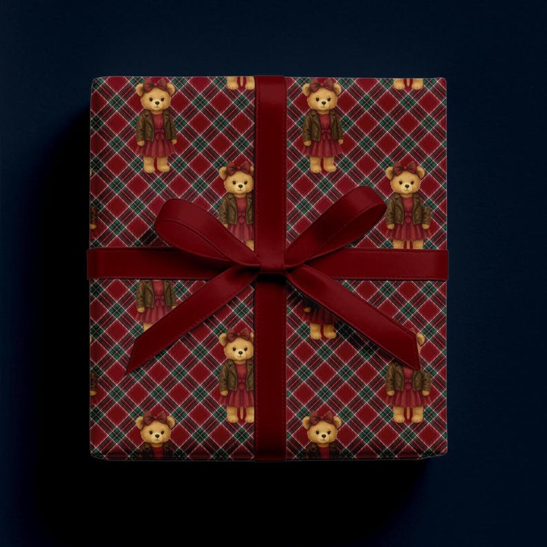 May include: A wrapped gift box featuring a red and green plaid pattern with repeating illustrations of teddy bears wearing dresses and jackets. The box is tied with a dark red ribbon and bow, creating a festive and decorative presentation.