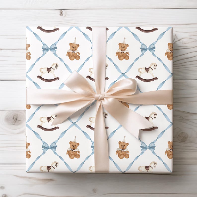 K&ouml;nnte beinhalten: Geschenk verpackt mit wei&szlig;em Hintergrund, verziert mit einem Muster aus braunen Teddyb&auml;ren und Schaukelpferden, hellblauen B&auml;ndern und Schleifen. Eine gro&szlig;e, hellbeige Satinschleife ziert die Oberseite.