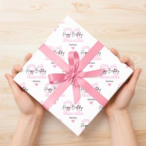 May include: White gift wrap with a pink and black pattern. The pattern features the number 21 with the words "Happy Birthday" and the name "Zachary".