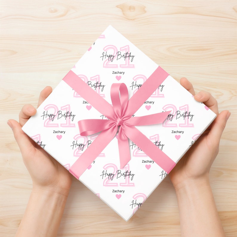 May include: White gift wrap with a pink and black pattern. The pattern features the number 21 with the words "Happy Birthday" and the name "Zachary".