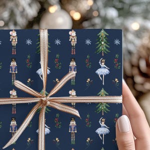 May include: Navy blue wrapping paper with a festive pattern of nutcrackers, mice, ballerinas, and Christmas trees. A gold ribbon is tied around the paper. The design is perfect for holiday gifts.