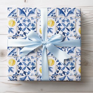 May include: A gift box wrapped in blue and white patterned paper with a light blue ribbon. The paper features a repeating pattern of lemons and blue and white tiles.