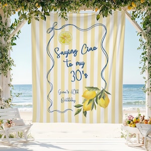 May include: A yellow and white striped backdrop with the text "Saying Ciao to my 30's" and "Gina's 40th Birthday" in blue script. The design includes a lemon slice and lemon branch illustrations. The backdrop is set up on a beach.