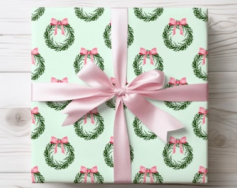 May include: A wrapped gift with light green wrapping paper featuring a pattern of green wreaths with pink bows. A pink satin ribbon is tied around the gift in a bow.