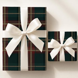 May include: Two wrapped gifts with a plaid pattern in dark green, red, and tan. Each gift is tied with a wide, white satin ribbon and bow. The gifts are on a white background.