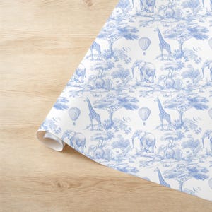 May include: Blue and white wrapping paper with a repeating pattern of giraffes, elephants, and hot air balloons. The pattern is reminiscent of a toile design.