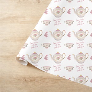 May include: White wrapping paper with a repeating pattern of pink teapots, teacups, and hearts. The text "Time for tea with the bride to be" is repeated throughout the pattern.