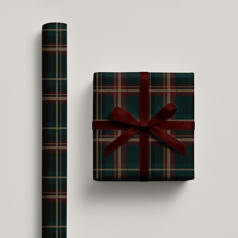 May include: A roll of wrapping paper and a wrapped gift box. Both feature a dark green, red, and tan plaid pattern. The gift box is tied with a dark red ribbon and bow. The wrapping paper is rolled up.