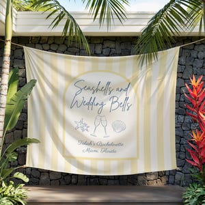 May include: A banner with vertical yellow and white stripes, featuring the text "Seashells and Wedding Bells" in a decorative font. The banner includes illustrations of a starfish, champagne flutes, and a seashell. The text "Taliah's Bachelorette Miami, Florida" is also present.