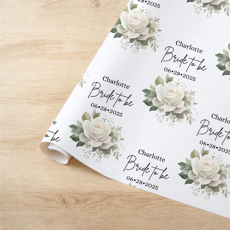 Peut inclure: Papier d'emballage floral blanc avec un motif r&eacute;p&eacute;t&eacute; de roses blanches et de feuilles vertes. Le texte "Charlotte Bride to be 06-28-2025" est r&eacute;p&eacute;t&eacute; sur le papier.