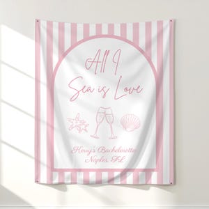 May include: A pink and white striped wall tapestry with the text "All I Sea is Love" in a cursive font. The design includes illustrations of a starfish, champagne flutes, and a seashell. The text "Kerry's Bachelorette Naples, FL" is also included.