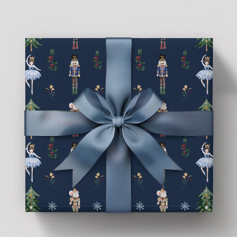 May include: A wrapped gift with navy blue wrapping paper featuring a pattern of nutcrackers, ballerinas, and Christmas trees. A wide, light blue satin ribbon is tied in a large bow around the gift.