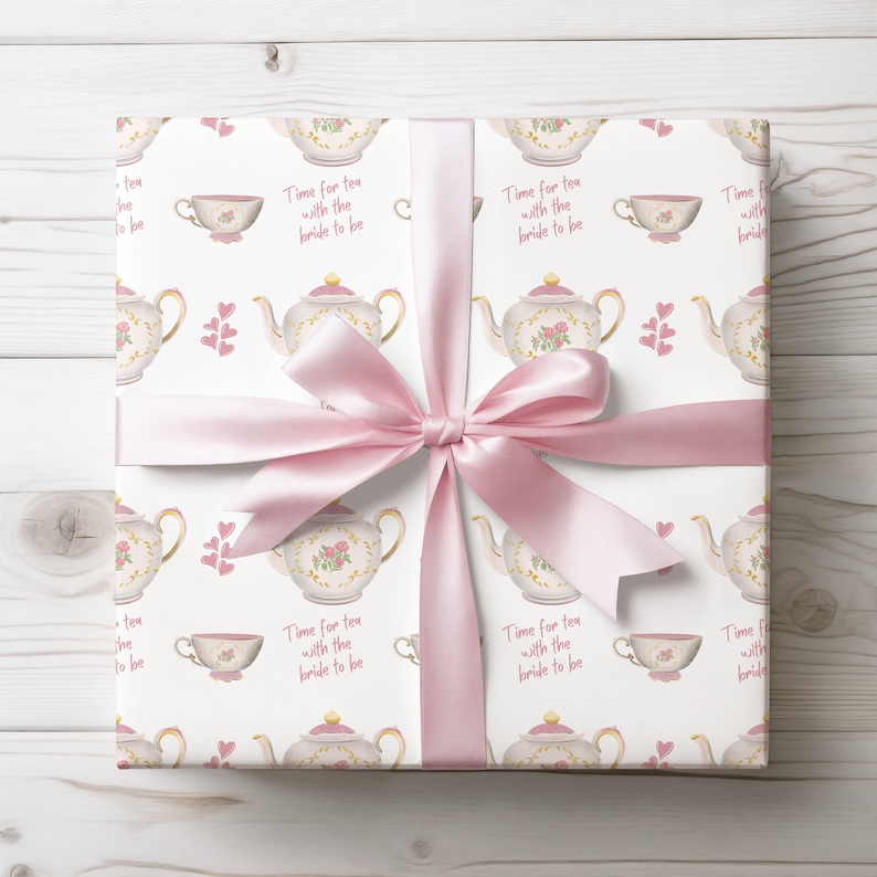 May include: White gift wrap with a pink ribbon. The wrap features a repeating pattern of teapots, teacups, and hearts. The text "Time for tea with the bride to be" is repeated throughout the pattern.